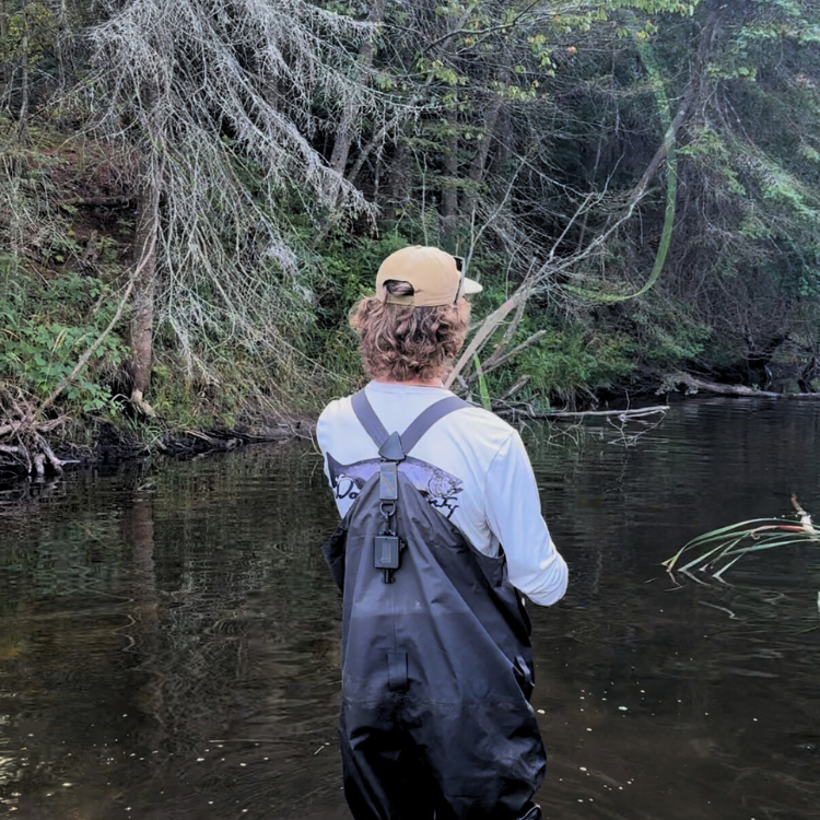 Fisherman wearing UPF Sunshirt in creek around woods with fly rod and waders on 